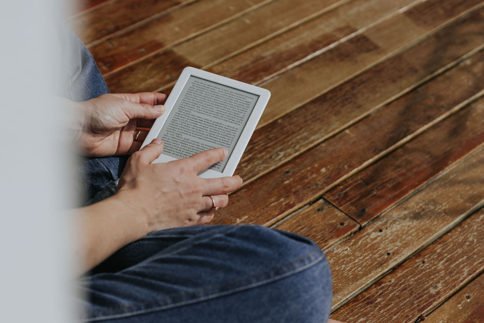 Hands holding an e-reader above a wooden floor