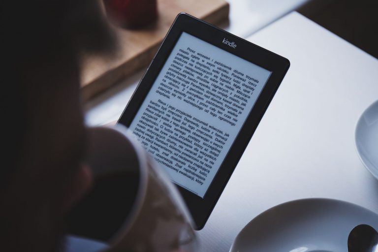 A person reading on an e-reader while holding a cup of coffee
